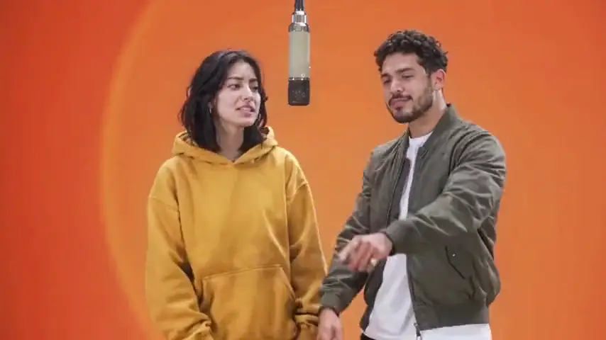 A woman in a yellow hoodie and a man in an olive bomber at the mic